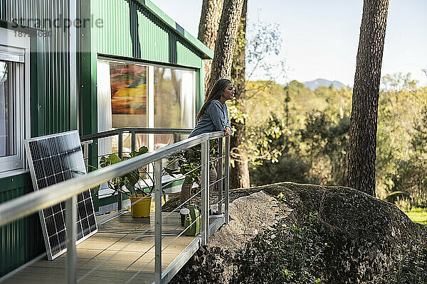 Nachdenkliche Frau steht auf der Veranda ihres neuen Zuhauses und blickt auf die Aussicht