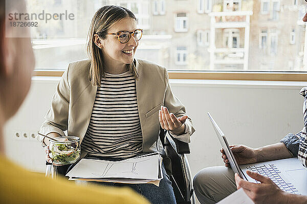 Lächelnde junge Geschäftsfrau im Rollstuhl bei einem Meeting im Büro