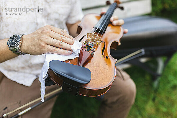 Hand des Geigers putzt Geige mit Lappen im Park