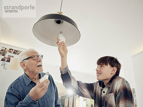 Enkel und Großvater tauschen alte Glühbirne gegen eine LED-Energiesparlampe aus