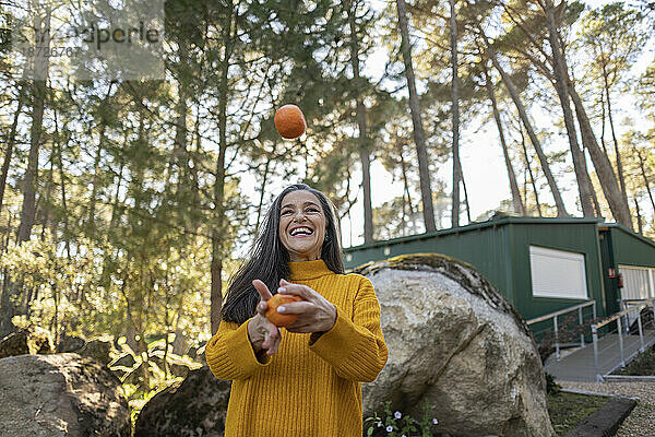 Reife Frau steht im Garten und jongliert mit Bio-Orangen