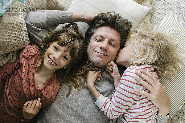 Glücklicher Vater liegt mit Töchtern zu Hause auf Kissen
