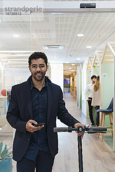 Geschäftsmann mit Elektroroller und Mobiltelefon im Büro