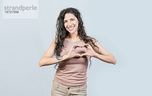 Lächelnde junge Frau macht Herzform mit ihren Händen. Teenagermädchen macht Herzform mit ihren Händen  Happy girl making heart shape with hands isolated