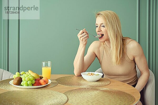 Frau mittleren Alters isst zu Hause Müsli mit Früchten