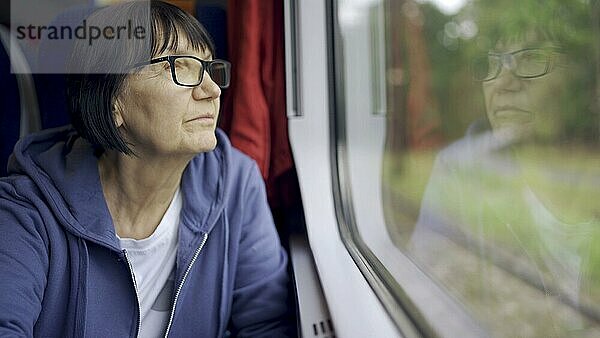 Ältere Dame mit Brille reist im Zug und schaut aus dem Fenster  das sich im Glas spiegelt