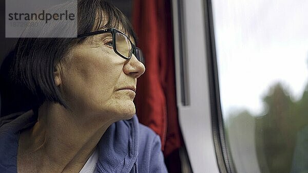 Ältere Dame mit Brille reist im Zug und schaut aus dem Fenster