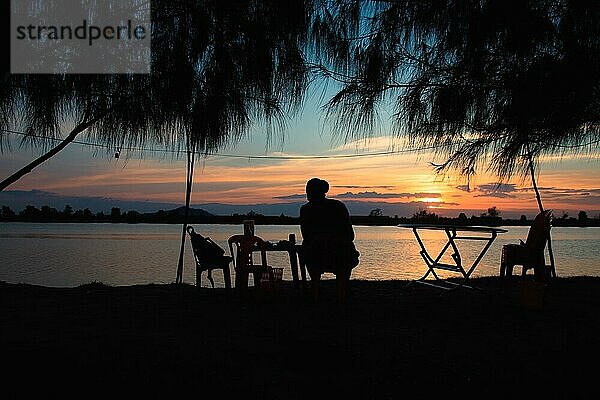 Silhouette eines Mannes  der den Blick auf den Sonnenuntergang am Flussufer in Kampot  Kambodscha  genießt  Asien