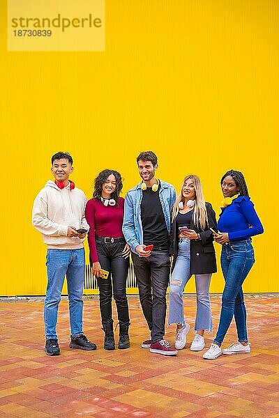 Porträt einer Gruppe lächelnder junger multiethnischer Teenager-Freunde  die Handys auf einem gelben Hintergrund benutzen. Technologie süchtig Millennial Gemeinschaft Konzept