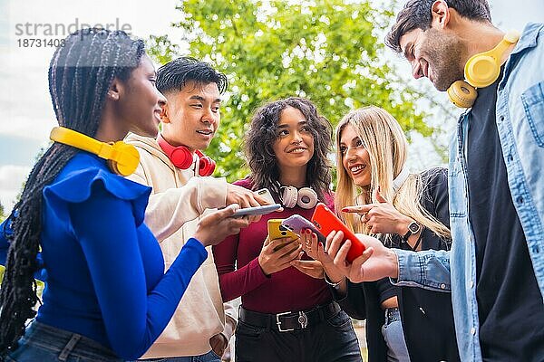 Gruppe junger lächelnder multiethnischer Freunde  die auf dem Campus in der Stadt Handys benutzen. Technologie süchtig Millennial Gemeinschaft Konzept. Social Media Kommunikation Generation Z