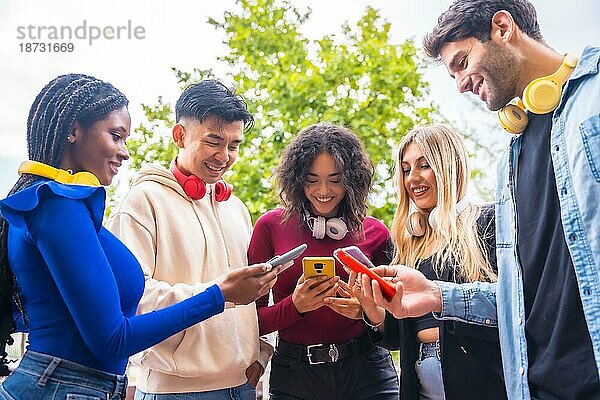 Niedriger Blickwinkel auf eine Gruppe junger multiethnischer Teenager  die auf dem Campus in der Stadt Handys benutzen. Konzept einer techniksüchtigen Millennial-Gemeinschaft. Social Media Kommunikation Generation Z