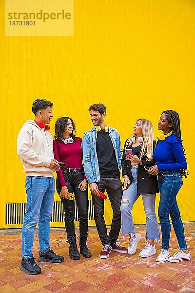 Porträt einer Gruppe lächelnder junger multiethnischer Freunde im Teenageralter  die Mobiltelefone auf einem gelben Hintergrund benutzen. Technologie süchtig Millennial Gemeinschaft Konzept. Social Media Kommunikation Generation Z