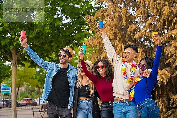 Gruppenbild von multiethnischen Freunden  die eine Party in einem Park feiern  Verschiedene junge Leute mit erhobenen Biergläsern bei einer Sommerparty  Happy Hour  Mittagspause und Jugendkonzept