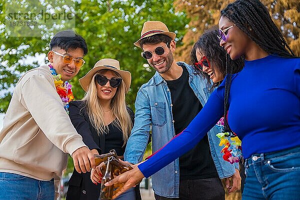 Multiethnische Freunde feiern in einem Park  Verschiedene junge Leute stoßen mit Glasflaschen Bier auf einer Party an  Jugendkonzept