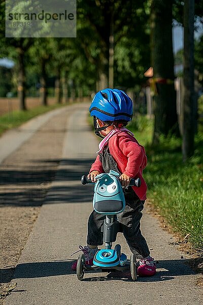 Ein kleines Kind mit einem blaün Fahrradhelm auf einem Motorroller