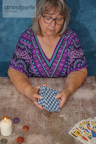 Frau mischt Tarotkarten auf einem Tisch mit Kerzen und Chakra Steinen