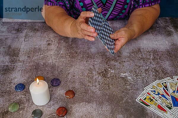 Frau mischt Tarotkarten auf einem Tisch mit Kerzen und Chakra Steinen
