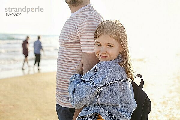 Liebevoller Vater umarmt seine entzückende kleine Tochter am Strand  Vater und Kind verbringen Zeit im Freien zusammen  sonniges Meer im Hintergrund. Parenting Konzept