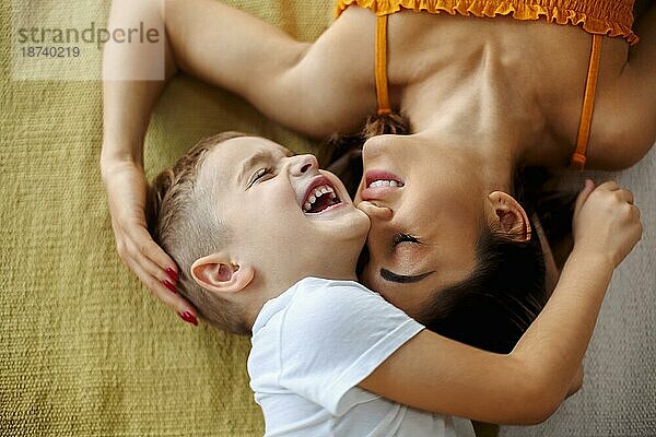 Blick von oben auf junge positive Familie Mutter und Sohn lachen und umarmen  während auf dem Bett liegend und genießen glückliche Momente zusammen  niedlichen kleinen Jungen verbringen Wochenende Tag mit Mama