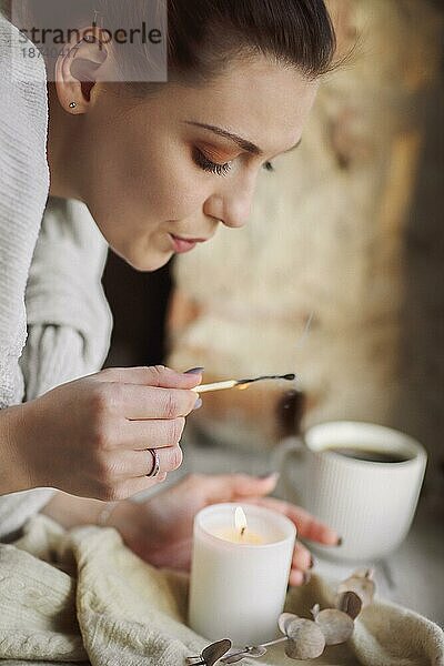 Weibliche Hände mit brennenden Streichholz Beleuchtung brennende Kerze auf der Fensterbank für Ruhe und Gemütlichkeit zu Hause  Frau versucht  gemütliche warme und intime Atmosphäre in der kalten Jahreszeit zu schaffen. Hygge Lebensstil Konzept