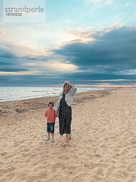 Junge liebende Mutter mit lächelnder Tochter  die ihre kleine Tochter am sonnigen Strand umarmt  glückliche Mutter umarmt kleines Mädchen und genießt die gemeinsame Zeit am Sommerstrand