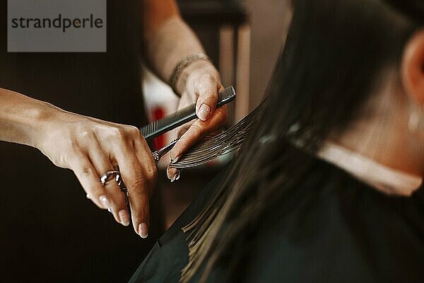 Friseurin mit Kamm und Schere zum Schneiden der Haare einer glücklichen Kundin während der Arbeit im Salon