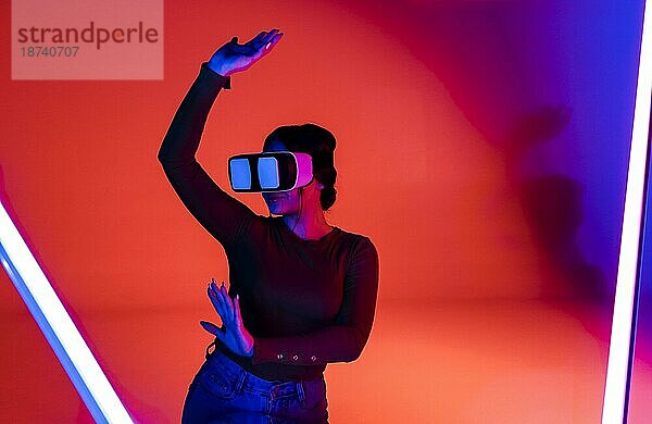 Glückliche Frau mit VRheadset lächelt und erkundet die virtuelle Realität unter roter Neonbeleuchtung in einem futuristischen Raum