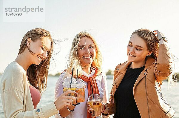 Glückliche junge Frauen mit Getränken zum Mitnehmen  die auf dem Bürgersteig spazieren gehen und an einem sonnigen Wochenendtag in der Stadt lächeln