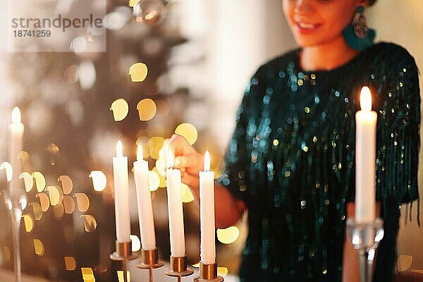 Eine unerkennbare Frau lächelt und zündet Kerzen an  während sie eine romantische Stimmung am Abend zu Hause schafft