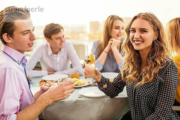 Glücklicher Mann und Frau mit alkoholischen Getränken  die lächelnd am Tisch sitzen  während sie sich mit einem Freund treffen