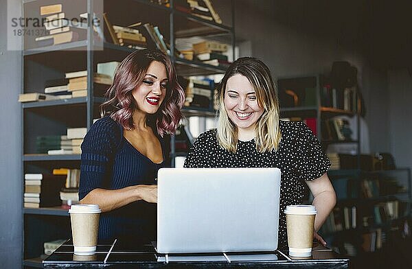 Glückliche Freundinnen lächelnd und machen Videoanruf auf Laptop am Tisch und genießen Kaffee in der Cafeteria
