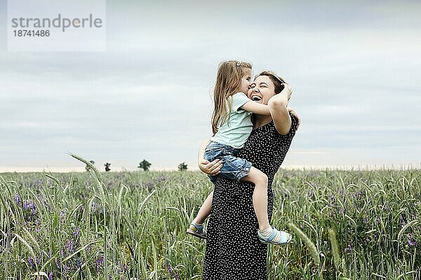 Glückliche Mutter und Tochter mit Feldblumenstrauß  die sich auf einer grünen Wiese umarmen. Mutter umarmt kleine Tochter im Freien auf einem Feld. Liebe und Familie Konzept