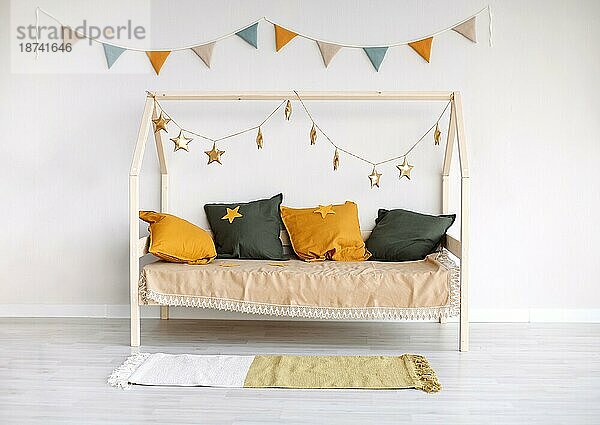 Stilvolles Kinderzimmer im Scandi Stil mit Montessori Bett  dekoriert mit bunten Kissen  Papierfähnchen und goldenen Sternen  die an einer Schnur hängen und für eine fröhliche Stimmung sorgen. Minimalistisches Kinderzimmer Design