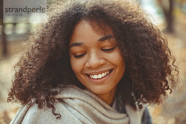 Cute Herbst Nahaufnahme Porträt der jungen lächelnd glücklich afrikanischen amerikanischen Frau mit lockigem Haar genießen Spaziergang im Park im Herbst Saison. Outdoorfoto von zufriedenen schwarzen Mädchen mit geschlossenen Augen in der Liebe mit dem Leben