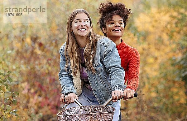 Zwei junge glückliche verschiedene weibliche beste Freunde fahren Fahrrad zusammen im Herbst Wald  aktive positive multirassische weibliche Freunde lächelnd in die Kamera  während stehend mit Stadt Fahrrad im Herbst Natur