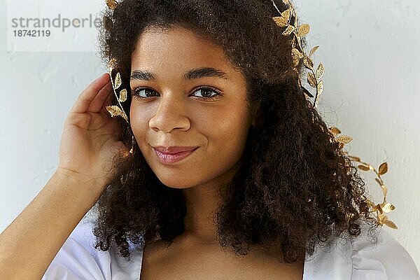 Close up Porträt der niedlichen afrikanisch amerikanischen Frau mit lockigem Haar in Blattgold Stirnband suchen flirty in die Kamera vor weißem Hintergrund  schöne Frau mit Melanin reichen Hautton. Natürliche afrikanische Schönheit