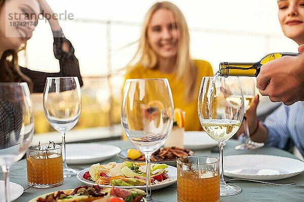 Fröhlicher Mann und Frauen lächelnd  während sie am Tisch sitzen und darauf warten  daß der Kellner beim Bankett Wein in die Kelche gießt