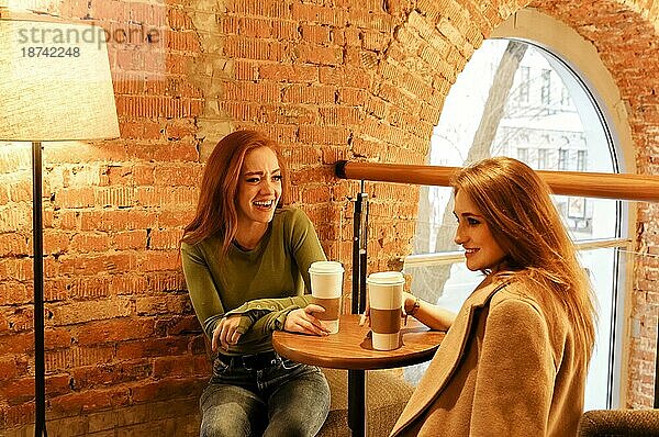 Glückliche junge multirassische Freundinnen sitzen am Tisch mit kalten Getränken in einem Café während der Mittagspause
