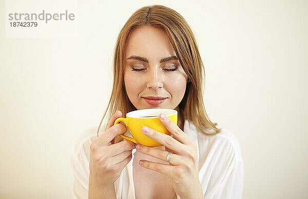 Erwachsene Frau im Bademantel  die die Augen schließt  während sie eine Tasse aromatischen  frisch gebrühten schwarzen Kaffee trinkt