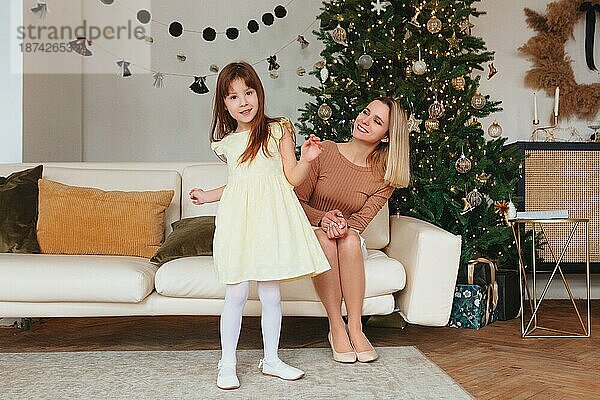 Glückliches verspieltes kleines Mädchen Tochter spielt mit positiven Mutter  verbringen Zeit zusammen während der Weihnachtsferien zu Hause  Mutter und Kind Spaß haben im Wohnzimmer mit Neujahr Baum
