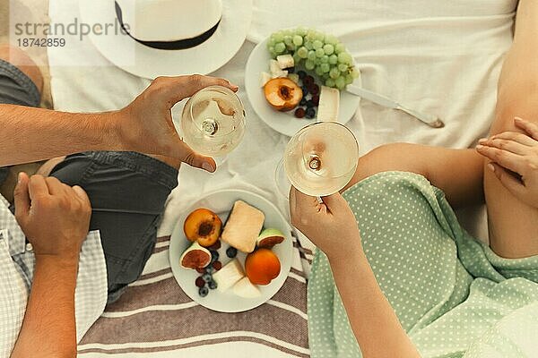 Draufsicht auf einen anonymen Mann und eine Frau mit Weingläsern  die bei einem romantischen Picknick am Strand auf die Früchte anstoßen