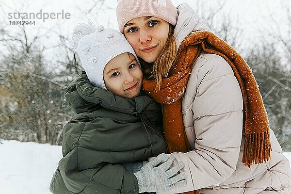 Lovely glückliche Familie Mutter und kleines Mädchen Tochter  die Spaß auf verschneiten Wetter im Freien  freudige spielerische Mutter mit Kind umarmen  während Zeit aktiv im Winter Park auf kalten frostigen Tag