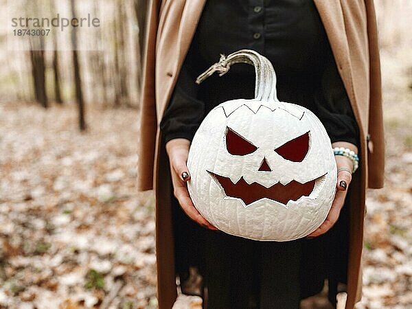 Close up Foto von jungen blonden Frau hält gruselig gestaltete weiße Kürbis  stehend isoliert über Herbst Wald Hintergrund. Herbstferien  Halloweendekorationen und Menschen Konzept