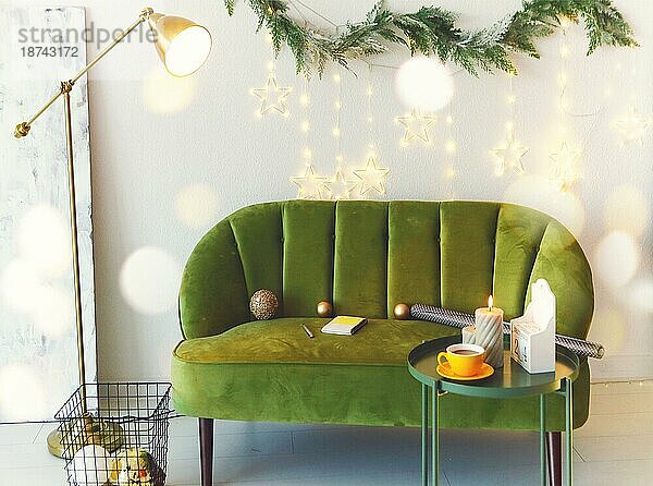 Stilvolle gemütliche und minimalistischen Stil Weihnachten Wohnzimmer mit grünen Velours Sofa gegen weiße Wand mit Tannenbaum Zweig Girlande und Weihnachtsbeleuchtung dekoriert  niemand. Modernes Appartement in der Weihnachtszeit