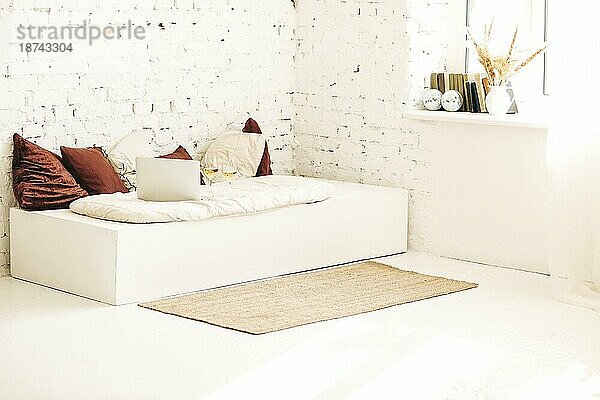 Matte in der Nähe der Couch mit Laptop und Wein gegen eine weiße Backsteinwand in einem sonnendurchfluteten Raum zu Hause