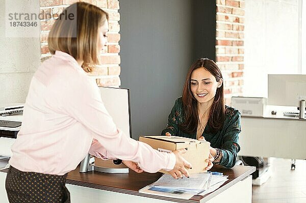 Fröhliche Managerin  die lächelt und einen Karton von einer Zustellerin entgegennimmt  während sie im Büro arbeitet