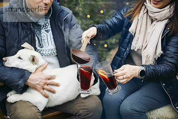 Lovely Paar mit niedlichen Hund sitzen auf Hinterhof außerhalb von jungen Nadelbäumen umgeben  lächelnd süß  während die Kommunikation mit einander auf frischen frostigen Luft  genießen Winterurlaub zusammen