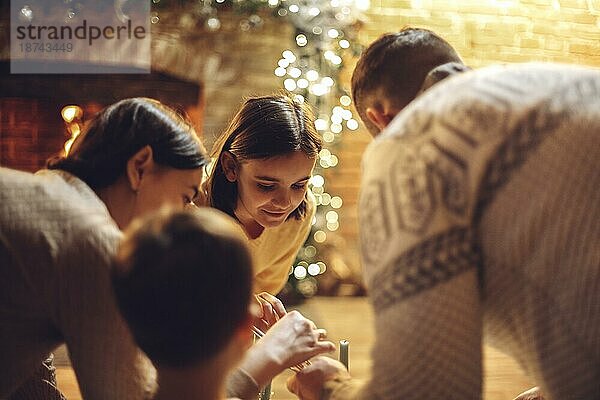 Glückliche Eltern mit Kindern genießen die Weihnachtszeit zu Hause. Vater  Mutter und Kinder in der Nähe von Kamin mit Weihnachtsbeleuchtung  Familie Toasting Marshmallows am Feuer zu Hause am Abend dekoriert. Selektiver Fokus