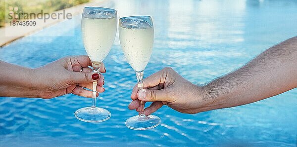 Ein Paar hält ein Glas Champagner und stößt am Pool an. Reisen und Urlaub Konzept
