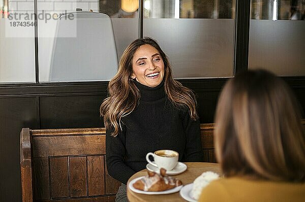 Zwei erfreute Frauen Freundinnen trinken Kaffee und reden in gemütlichen Café  lächelnd weiblichen besten Freunde genießen angenehmes Gespräch bei einem Treffen im Café. Freundschaft Konzept
